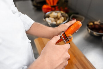 cooking food, profession and people concept - close up of male chef cook with knife peeling carrot at restaurant kitchen