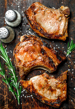 Grilled pork steaks with rosemary and salt on an old board.