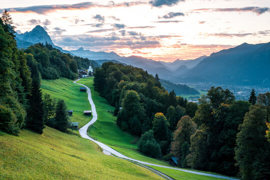 Straße, grüne Wiese und Kapelle zum Sonnenuntergang in den Bergen.