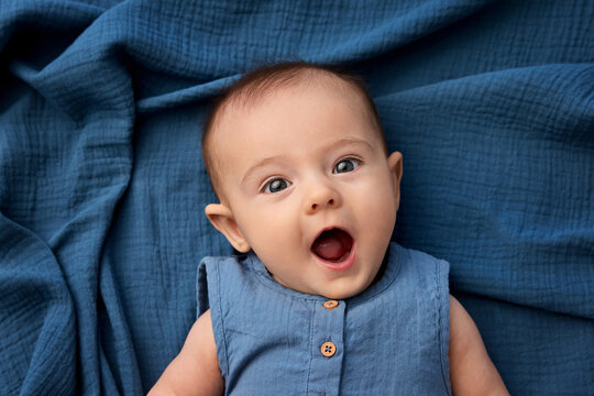 Portrait Of Funny Newborn Baby Lying On Blue Blanket Making Surprised Face