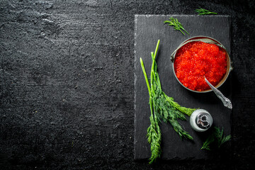 Fototapeta na wymiar Red caviar in a bowl on a black stone Board with salt and dill.
