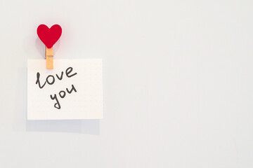 Love you note on white sheet of paper with heart-shaped magnet on the fridge.