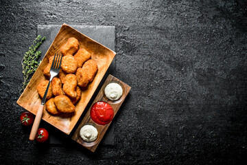 Chicken nuggets in a plate with fork, thyme and different sauces.