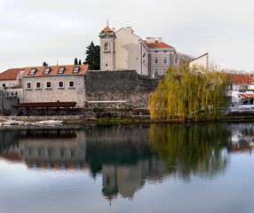Herzegovina museum also known as Muzej Hercegovine in old town of Trebinje with stone fortress wall  and tall tower under water surface of Trebisnjica river autumn landscape front view