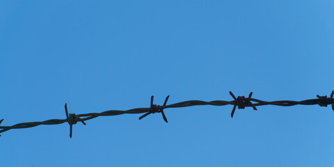 Metal barbed wire on a background of clear blue sky, close-up. Black barb wire under blue sky,...
