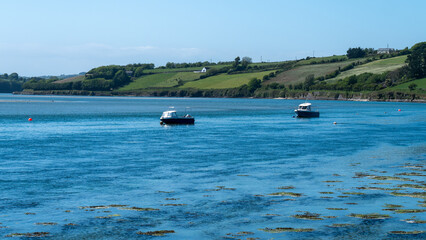 Two small boats are anchored in Clonakilty Bay on a spring day. Beautiful Irish seaside landscape. Clear sky and blue water, boats on blue sea.