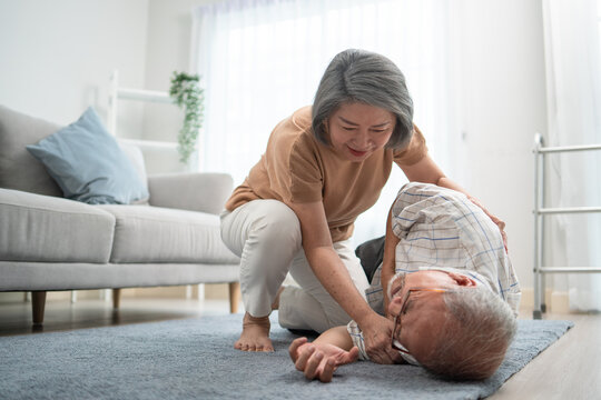 Asian senior wife helping husband fainting and falling on the ground in the living room. Elderly male patient having an accident or heart attack. home nursing and health insurance concept