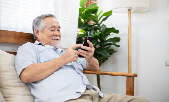 Senior man smiling and sitting on couch using smartphone watching funny clip, browsing, online shopping or video call chat with family. 