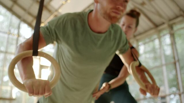 Fit young man doing push-ups using suspension ropes with a gym instructor during a workout