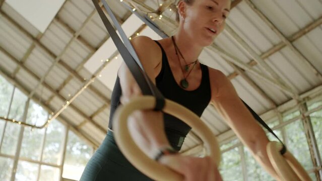 Fit focus woman hanging from suspension ropes during a workout session in a studio