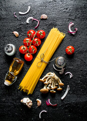 Raw spaghetti with onion slices, tomatoes, mushrooms and oil in a bottle.