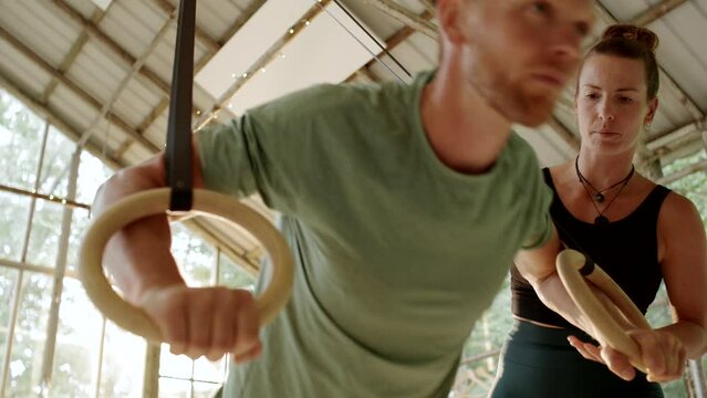 Fit young man doing push-ups using suspension ropes during a gym session with an instructor