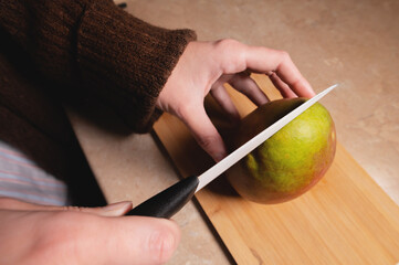 Fresh organic mango, woman cutting mango on wooden cutting board, preparing fruit salad for dinner