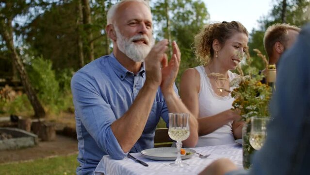 Mature man talking with family and friends during an outdoor lunch together on a summer afternoon