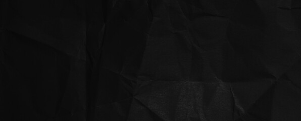 Black background of crumpled paper in the dark. Wide panoramic black background with space for design. Web banner, website header