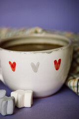 A cup of coffee, cocoa, chocolate with hearts on a lilac violet background. Marshmallows on a table. Cozy still life with hot drink made with love, sweets. February 14, Happy Valentines Day concept.