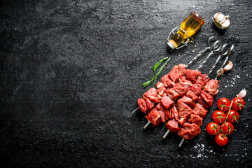 Raw kebab on skewers with tomatoes, garlic and oil in a bottle.