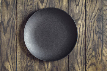 Empty black plate on oak wooden background. Top view, with copy space