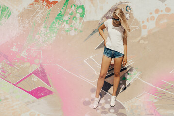 oung attractive and beautiful girl is standing on a graffiti wall background. Woman is wearing white, empty basic t-shirt without logo. Vertical mock-up.