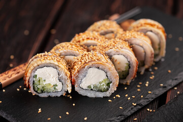 Japanese cuisine - sushi roll with cucumber and cream cheese topped with eel close-up on black board