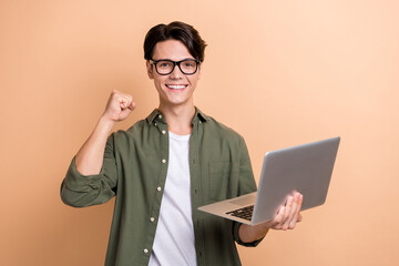 Photo of positive man use wireless netbook raise fist celebrate triumph isolated on beige color background