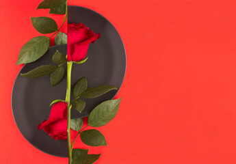 Red rose on the black plate on the red background. Copy space. Top view.