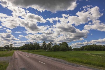 Gorgeous view of highway going into distance through forests against background of blue sky with white clouds. Sweden.