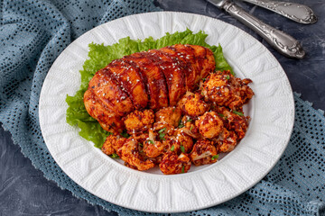 Oven baked Chicken breast and cauliflower in tomato sauce served on a plate. Selective focus, horizontal.