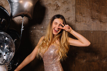 Happy excited cute woman with wavy long hair wearing golden dress smiling and posing at camera with...