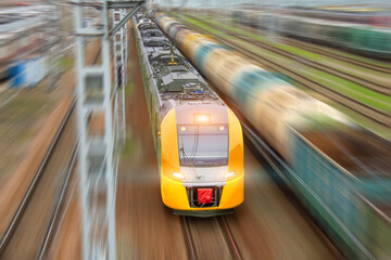 Suburban yellow electric train with passenger cars rushes along the railway track, aerial view.
