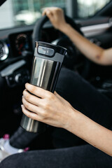 Fototapeta na wymiar thermo mug thermos in the hands of a woman in the car