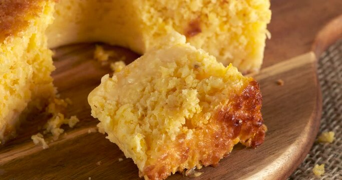 Homemade round cake made of green corn and cheese, known as "Pamonha Cake". Typical Brazilian food of Festa Junina(june festival) with a piece cut on a round wooden board on a rustic wooden table