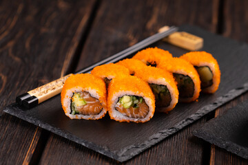 California sushi roll with salmon avocado, cucumber and tobiko caviar served on black board close-up - Japanese food