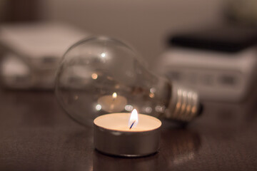 A burning candle against the background of a light bulb and power banks. Blackout due to war in...