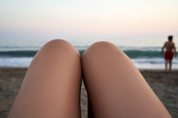 Female legs on the beach, with sea in the background