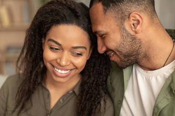 Obraz premium Loving african american man and woman bonding at home, embracing and smiling, black couple sitting on sofa