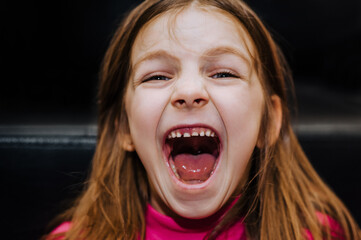 Close-up portrait of the face of a beautiful, red-haired, laughing girl, a child with an open mouth. Photography, emotions, concept.
