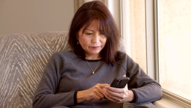 Attractive woman with dimples relaxing near window checks email on smartphone