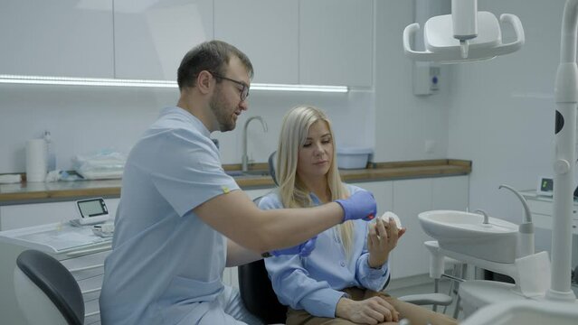 Man dentist shows patient girl how to properly brush her teeth in dental office. Dentist and patient talking about teeth with dentures