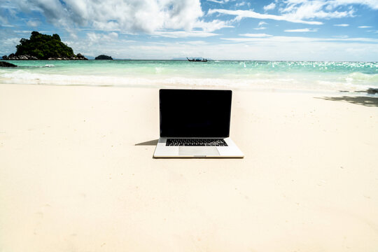 Computer notebook with empty black screen on the sandy tropical beach - digital nomad concept. © neonshot