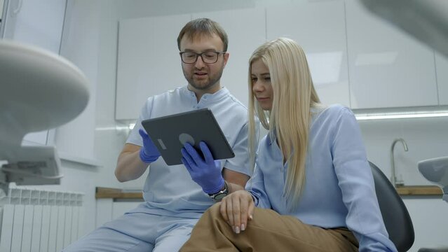 The dentist uses a tablet to show the patient images of the teeth in modern dental office. Painless dental treatment