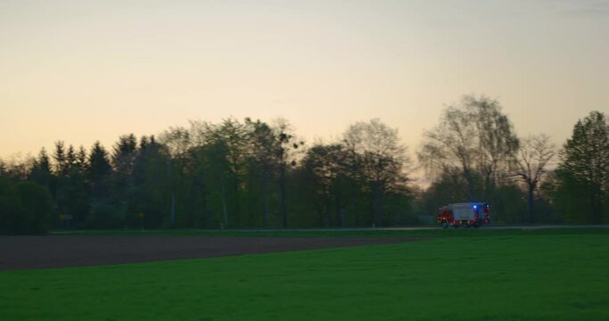 Feuerwehr f&auml;hrt mit Blaulicht auf Landstra&szlig;e in Abendstimmung