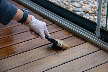 Deck staining, worker applying deck oil on decking boards with paint brush, hardwood terrace...