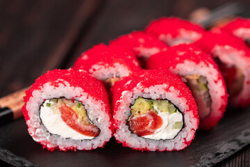California sushi roll with salmon, avocado cucumber and tobiko caviar served on black board close-up - Japanese food