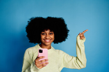 Cheerful black woman with smartphone pointing a side