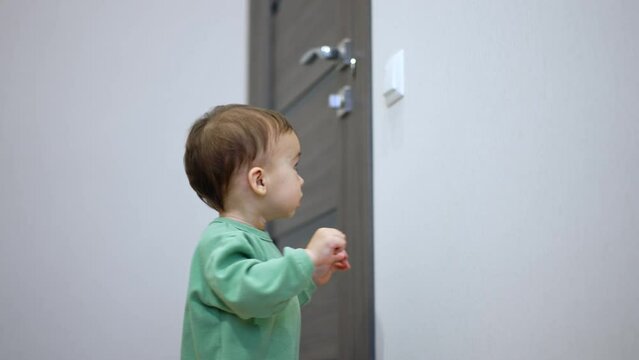 Nice little kid switches off the light in the room. Surprised toddler looks around the dark room.