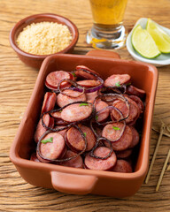 Grilled calabrese sausage portion with onion, lemon, farofa and beer over wooden table