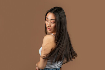 Young korean lady with perfect skin showing her long silky straight hair, posing on brown studio background, free space