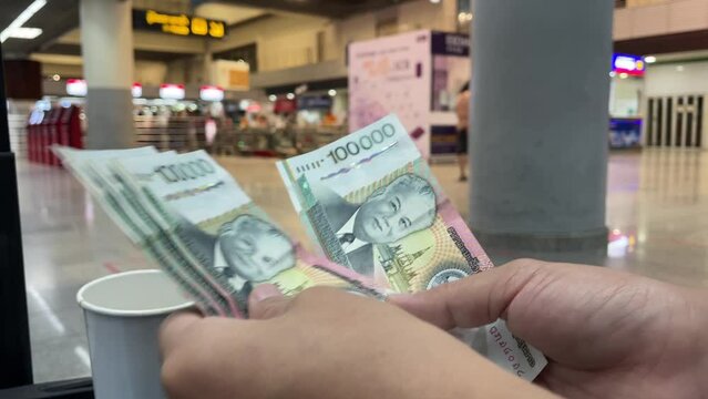 Bangkok, Thailand - Circa January, 2023 : Female hand counting 100000 lao kip money at the airport with blurred check in counters in background. Travel and tourism concept