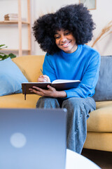 Obraz na płótnie Canvas Smiling black woman taking notes while attending a university online class